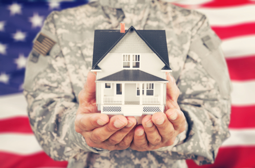 Military dressed person holding small house